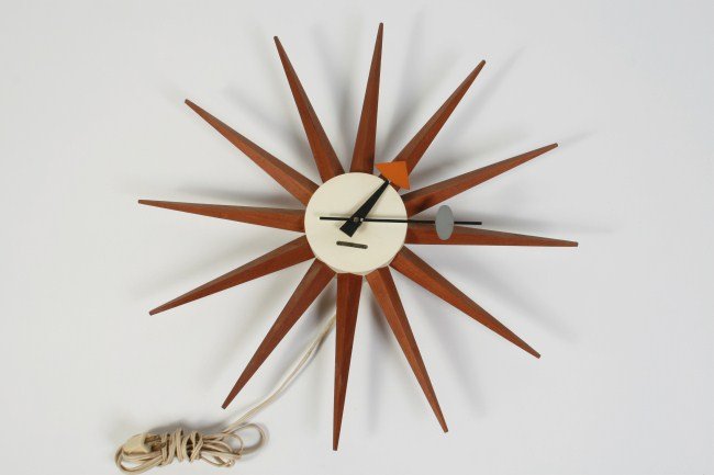 Howard Miller Spike Clock by George Nelson: George Nelson Spike wall clock. American, mid 20th century. Having natural wood spikes around a white enameled metal dial, black, gray and orange hour hands. Made by Howard Miller. Label affixed to di