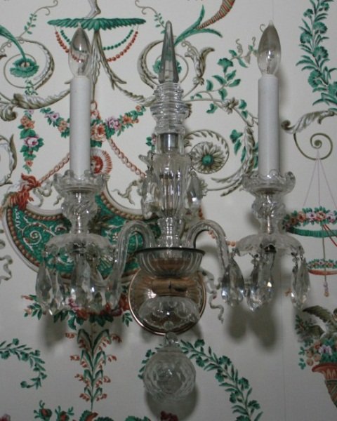 Two-Light Crystal Sconce, 20th C.: Two-light crystal sconce. American, 20th century. Two-light crystal sconces hung with prisms and with central spire. Height 13", width 11". Condition: Appears fine.