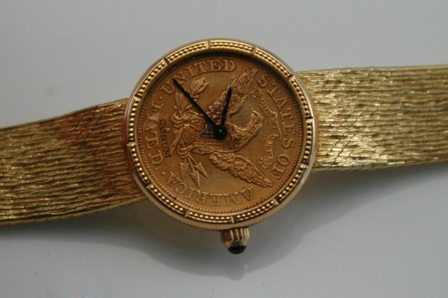 18K Gold Corum $20 Liberty Coin Wristwatch: 18 karat yellow gold Corum wristwatch with 1903 Liberty $20 gold coin face. Swiss, 20th century. 18 karat yellow gold band, dial of sapphire crystal and with black baton hands. With quartz movement. S