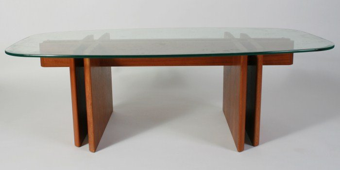 Trekanten Glass Top Coffee Table by Gustav Gaarde: Trekanten glass top coffee table. Mid-century. Designed by Gustav Gaarde. Oblong glass top with beveled edges supported by interlocking teak base. Unmarked. Height 17", width 56", depth 31".