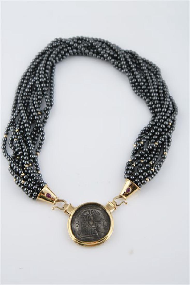Ladies 18k Yellow Gold Antique Coin Necklace: One ladies antique coin and hematite bead necklace made of 18k yellow gold. Necklace is set with one (1) antique coin and two (2) cabochon rubies, all bezel set. Necklace is 16 inches long. Weighing 2