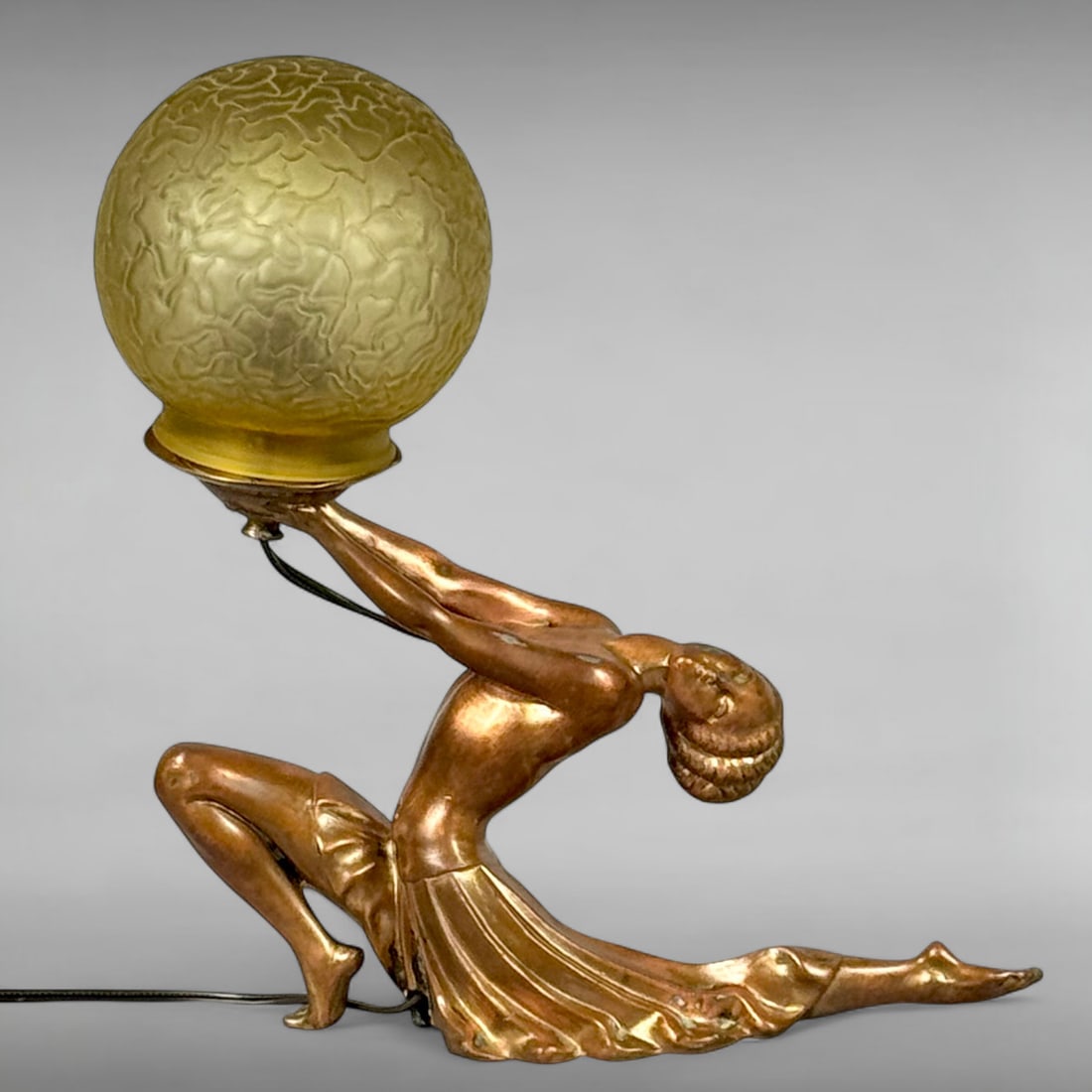 Vintage Art Deco Frankart Style Figural Table Lamp with Female Dancer Holding Crackle Glass Globe: This striking vintage table lamp exemplifies Art Deco sophistication. It showcases a sculpted female dancer in a dynamic pose, her arms elegantly uplifted to support a spherical amber crackle glass sh