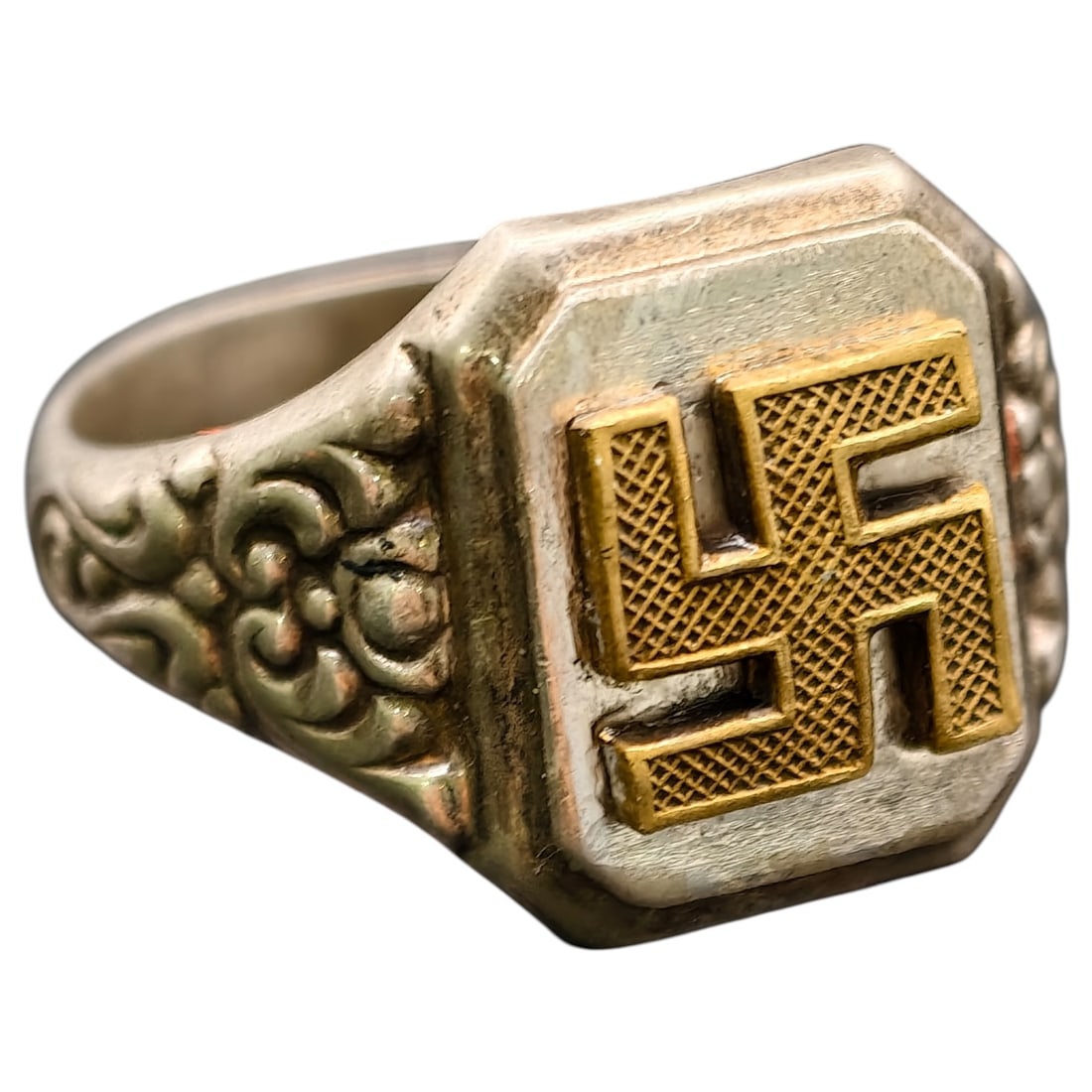 NSDAP Sympathizers Ring 835 Silver: A ring in what appears to be silver featuring a raised, textured gilt-metal swastika applied to an octagonal bezel, flanked by scrolling repoussé foliate decoration on the shoulders.Rings of this
