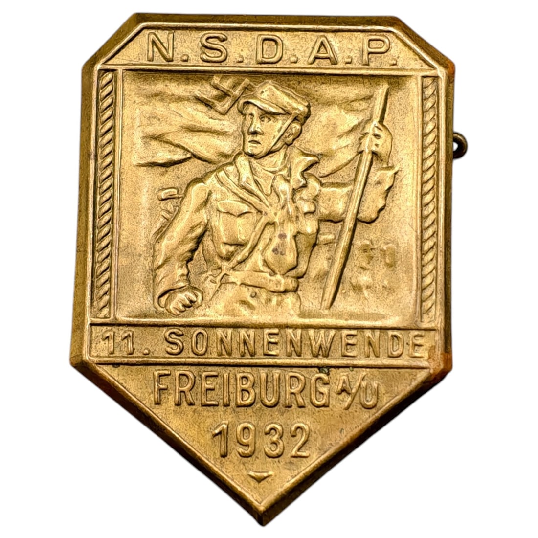 German NSDAP 1932 "11. Sonnenwende Freiburg" Tinnie Badge: A pre-1933 period NSDAP commemorative tinnie/badge marking the '11. Sonnenwende' (Solstice) event held in Freiburg im Breisgau in 1932. The obverse depicts a marching SA-type figure carrying a flag, w