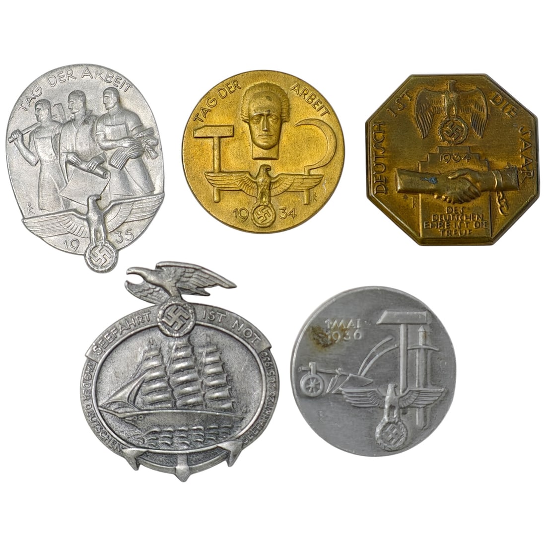 Nazi Third Reich Tinnie Event Badges: A set of commemorative tinnie badges from the 1930s, including two 'Tag der Arbeit' (May Day) badges dated 1934 and 1935, a 'Deutsch Ist Die Saar' octagonal badge dated 1934, a 'Seefahrt Ist Not' mari