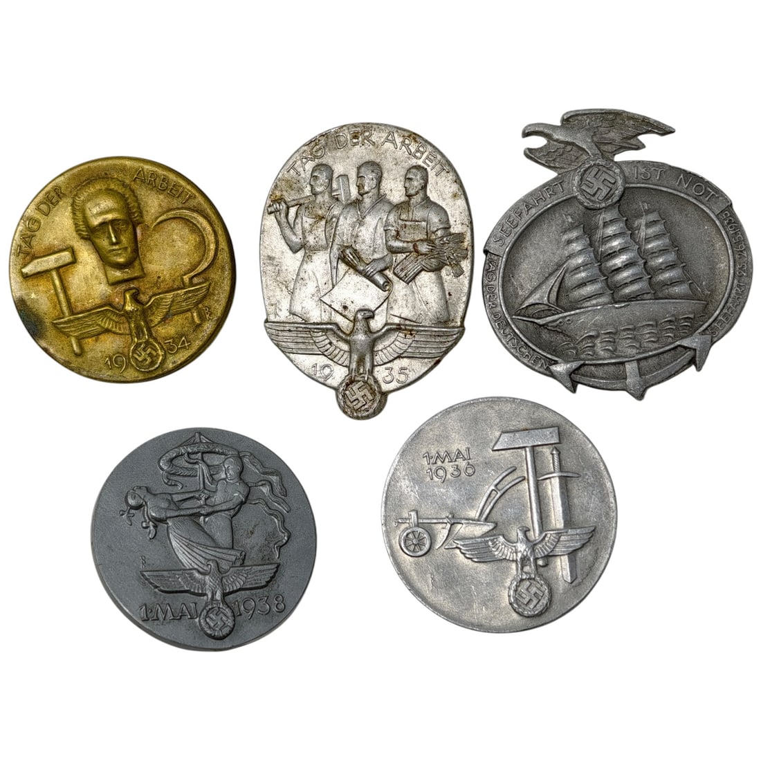 Third Reich Nazi Set of Tinnie Badges: A set of pin-back tinnie event badges commemorating National Socialist observances, including 'Tag der Arbeit' (May Day) 1934, 1935, and 1938 examples, a 1 Mai 1930 agricultural-themed badge, and a ma