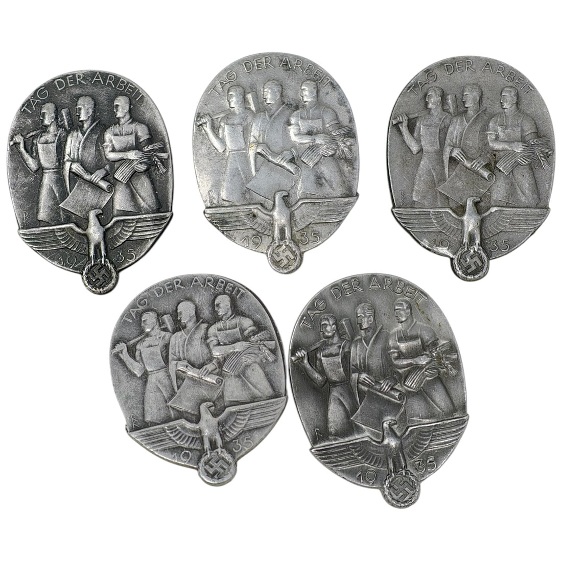 German 1935 'Tag der Arbeit' (Labor Day) Tinnies - Set: A set of oval pinback tinnie badges commemorating May Day 1935, each depicting three workers with tools and a sheaf of wheat above a stylized eagle with swastika, inscribed "TAG DER ARBEIT" and dated
