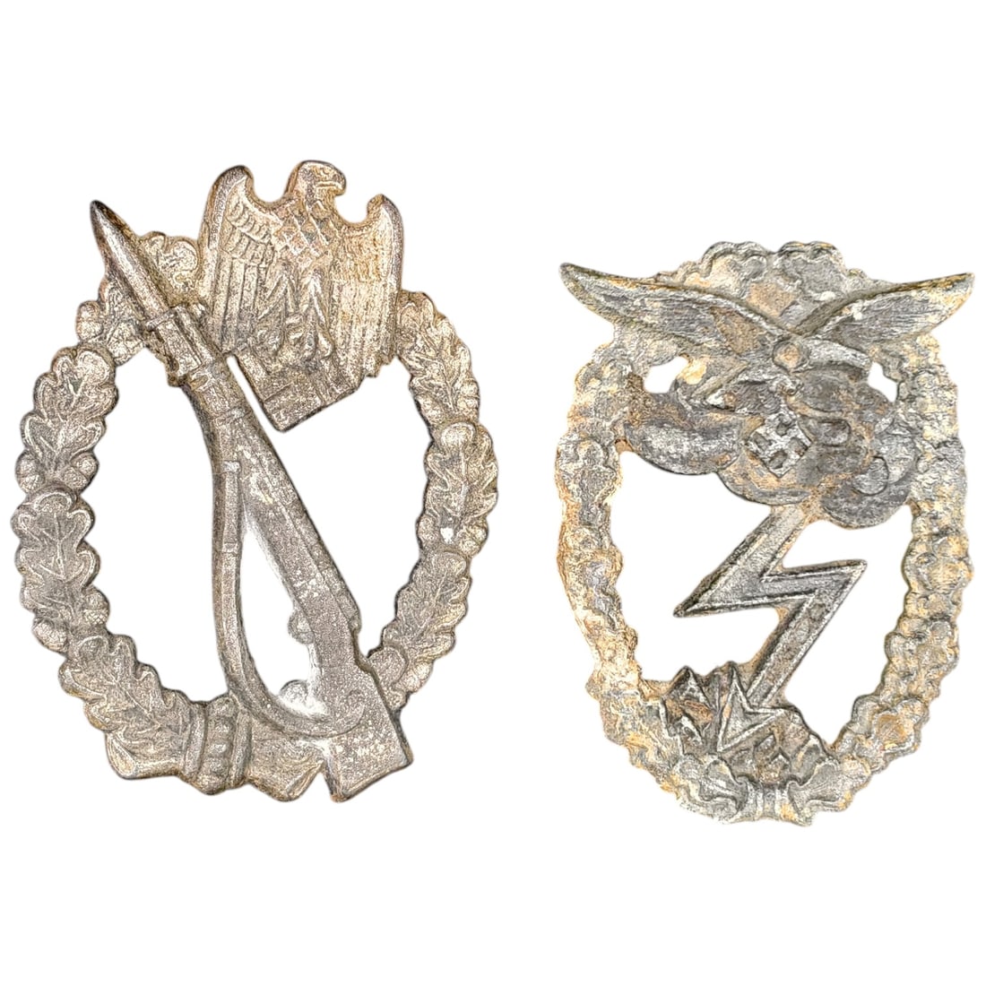 Third Reich Infantry Assault Badge and Luftwaffe Ground Assault Badge (Pair): A pair of Third Reich era badges in what appears to be zinc. The first is an Infantry Assault Badge, depicting an eagle atop a crossed bayonet and rifle within an oak leaf wreath, in a finish that app