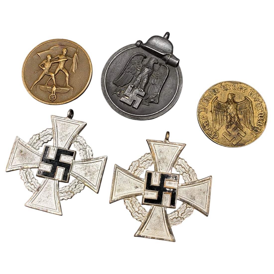 German WWII Era Mixed Medal Lot: A mixed lot of German WWII-era items: a set of 'Für Treue Dienste' (Faithful Service) crosses with a finish that appears to be white and black-painted swastika centers within wreaths; a tinnie in wha