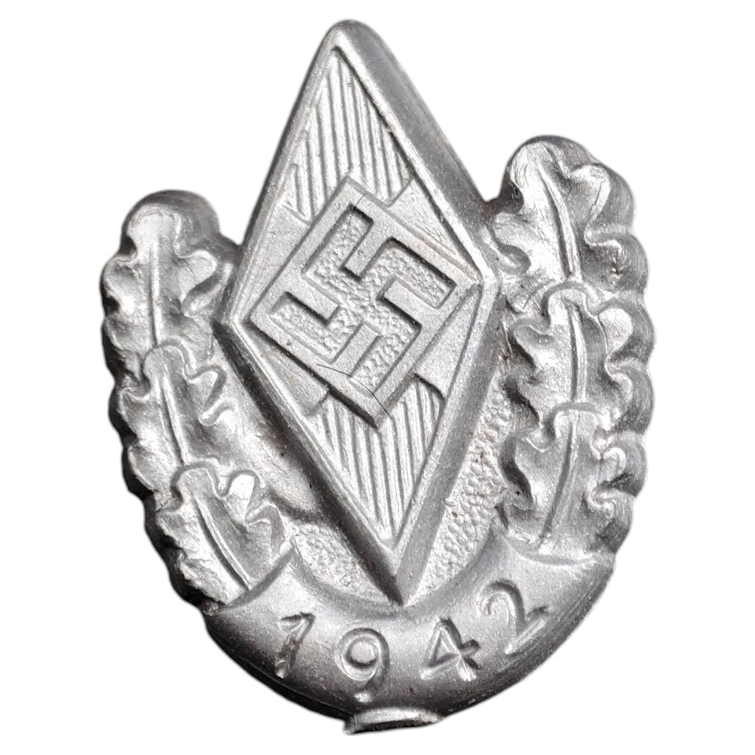 German WWII Hitler Youth HJ Badge: Cast metal badge featuring a diamond-shaped HJ (Hitler-Jugend) emblem set within an oak leaf wreath, with the date '1942' at the base. Surface shows a silvered/pewter-toned finish.