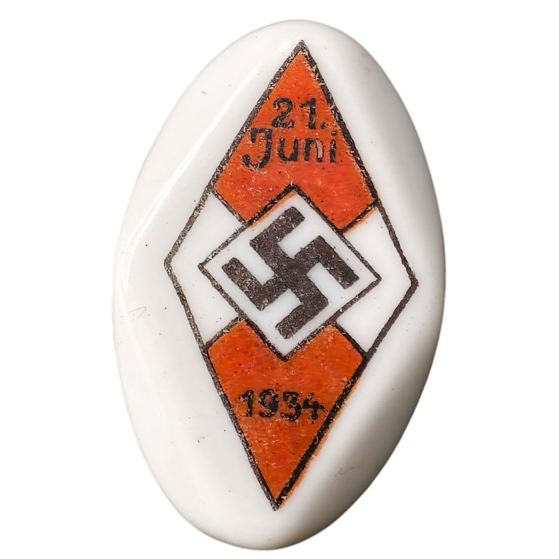 Hitler Youth 21 Juni 1934 Badge: A porcelain oval tinnie-style badge commemorating a Hitler Youth event dated 21. Juni 1934. The badge depicts a stylized diamond motif with a central mobile swastika flanked by orange painted panels, 