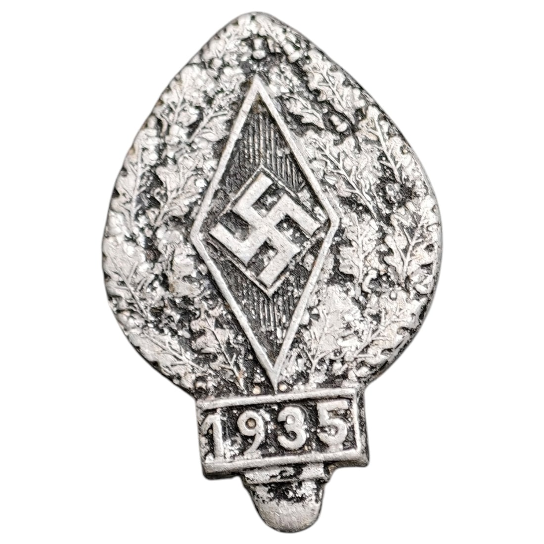 Hitler Youth HJ Jugend 1935 Badge: A leaf-shaped white-metal HJ member's badge featuring an oak leaf wreath surrounding a central diamond with swastika, dated "1935" on a banner at the base. The reverse bears a maker mark reading "OVER