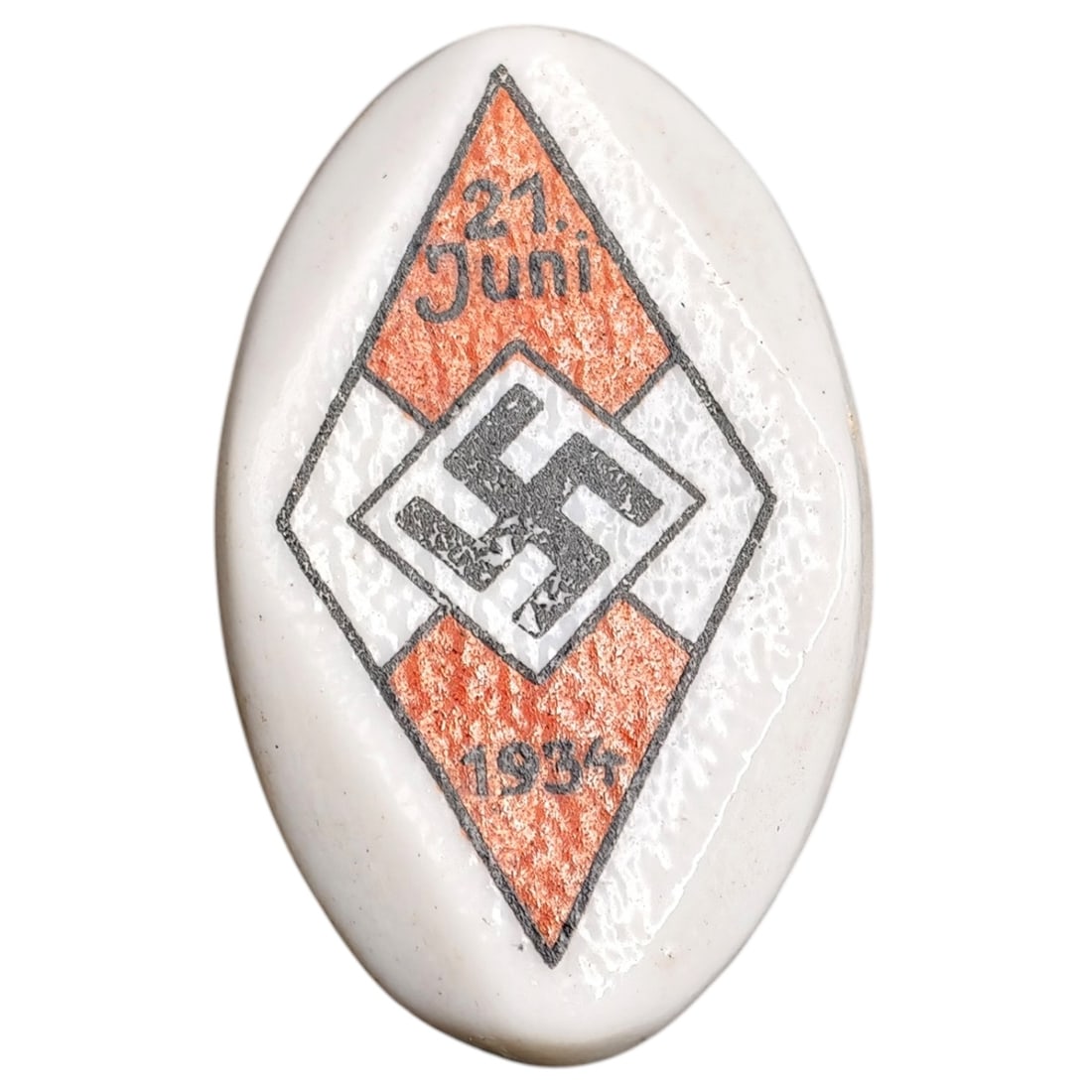 Hitler Youth 21 Juni 1934 Badge: Oval celluloid/porcelain-style membership badge with painted diamond design featuring an orange lozenge, central swastika, and inscription "21. Juni 1934," marking a Hitler Youth (Hitlerjugend) event.
