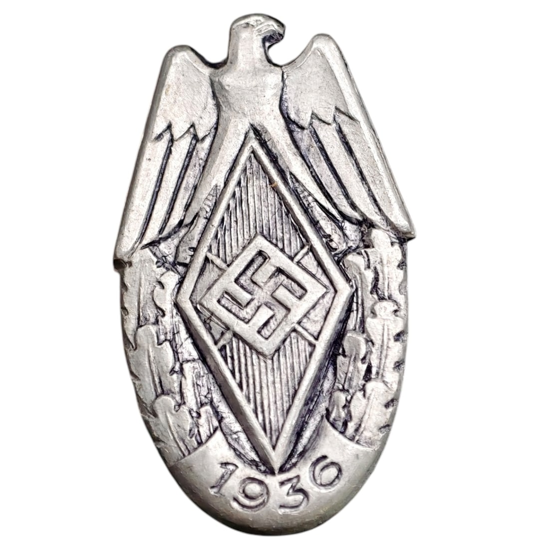 German WWII Hitler Youth HJ Badge: A stamped tinnie badge in what appears to be white-metal featuring an eagle above a diamond-shaped device with swastika, flanked by laurel/oak leaves, dated 1936 at the base. The reverse retains the m