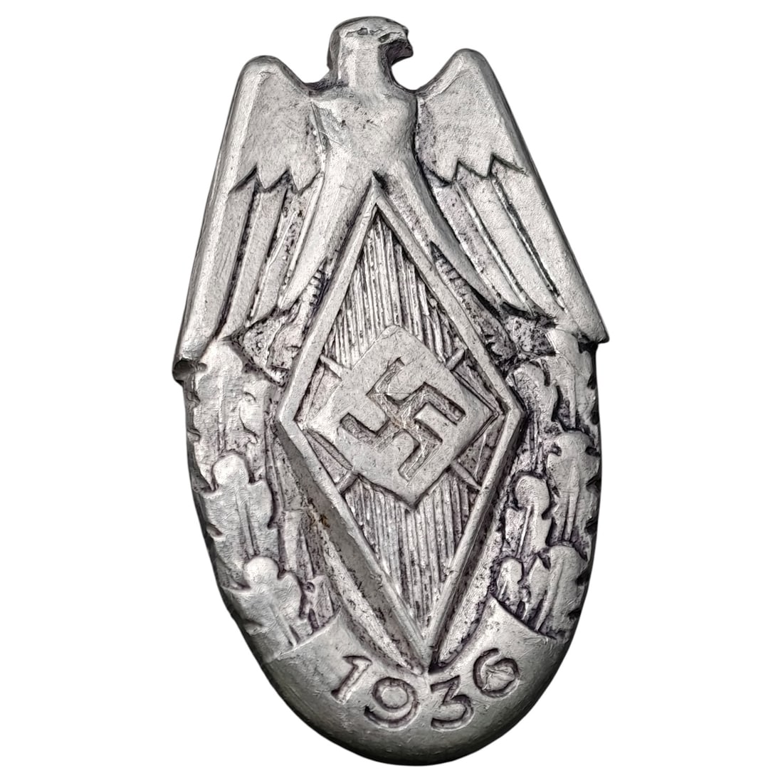 German WWII Hitler Youth HJ Badge: A shield-shaped tinnie badge featuring a stylized Reich eagle atop a diamond-shaped HJ emblem, dated 1936 at the base. Reverse maker-marked with a stamped inscription reading "Hillenbrand & Bruck, Lud