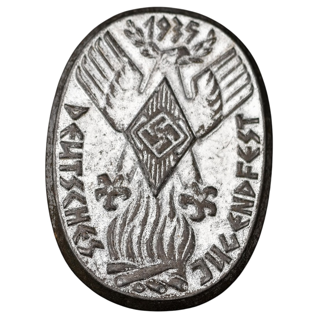 Third Reich 'Deutsches Jugendfest' 1935 Tinnie Badge: Oval stamped-metal commemorative badge (tinnie) inscribed 'Deutsches Jugendfest' with date '1935', depicting an eagle with outstretched wings above a diamond-shaped device and a bonfire. Likely worn o