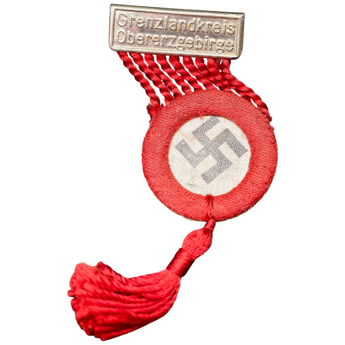 NSDAP Grenzlandkreis Obererzgebirge Pin: A stickpin-style tinnie/rally badge with a stamped tab in what appears to be metal reading 'Grenzlandkreis Obererzgebirge', attached by red twisted cord to a cloth rosette centered with a printed