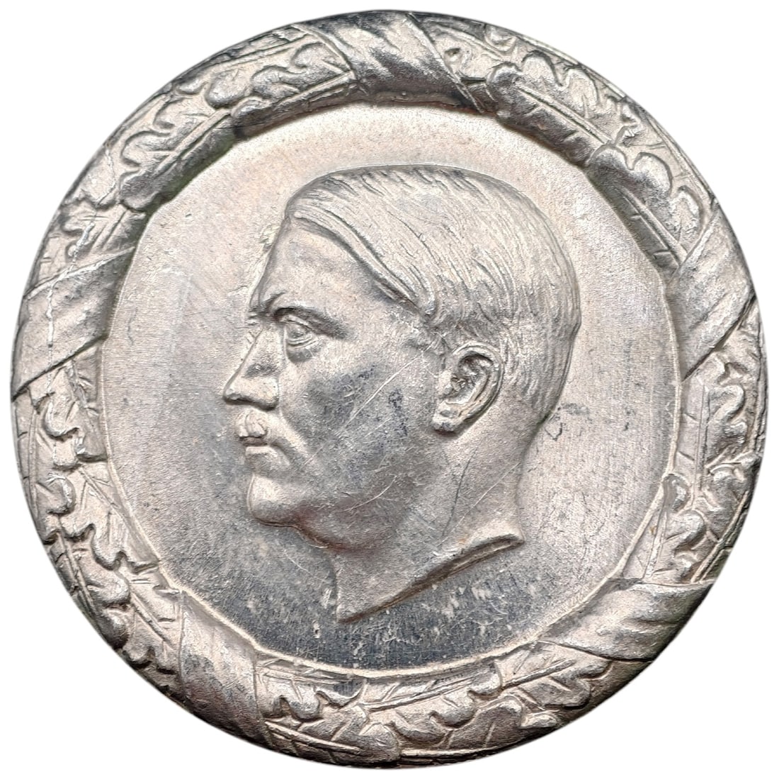 Adolf Hitler Badge: A round pin-back donation badge (WHW - Winterhilfswerk) featuring a profile portrait bust, surrounded by an oak leaf wreath border. The reverse is marked 'AMTLICH GENEHMIGT' (officially approved), 'W.