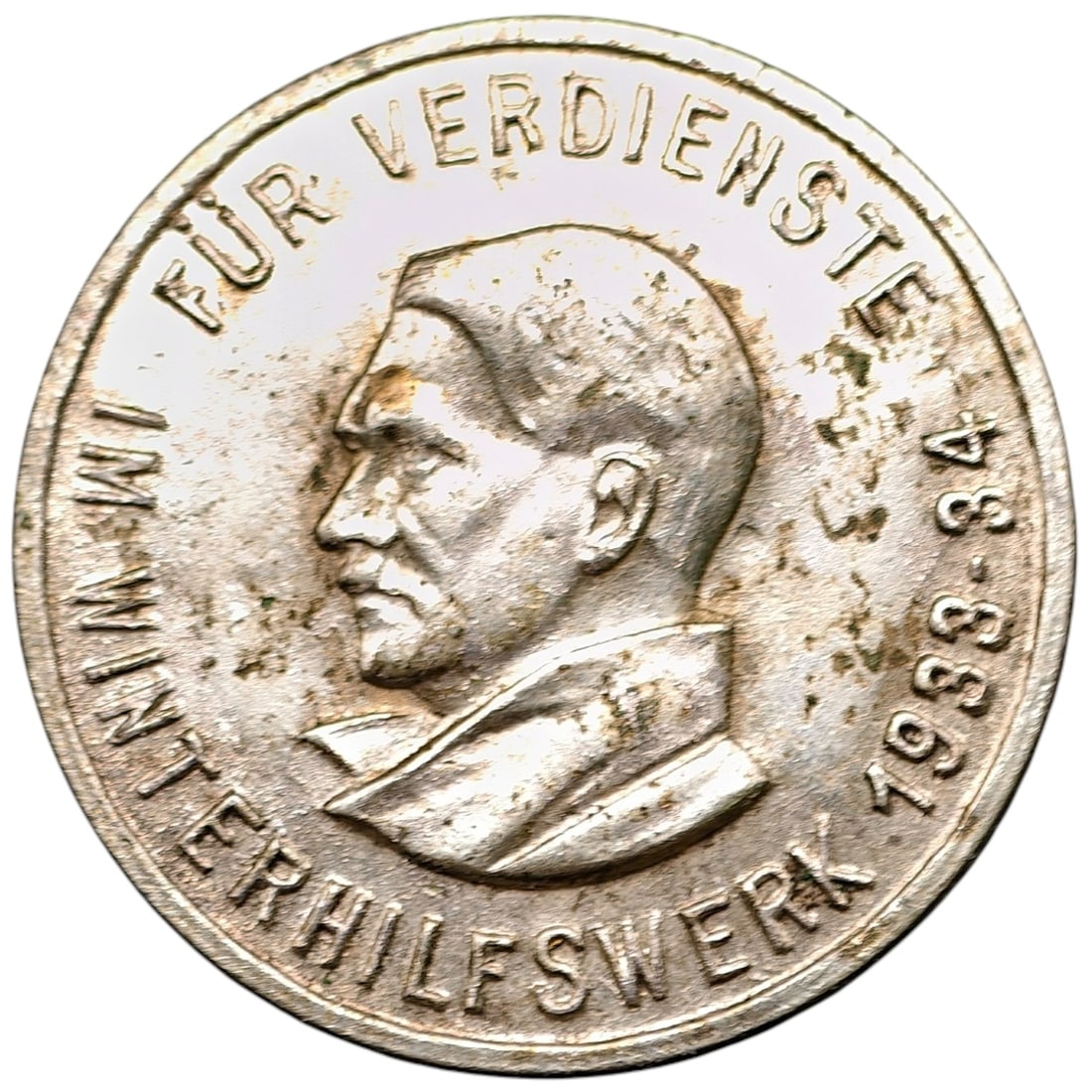 Adolf Hitler WHW 1933-34 'Für Verdienste' Pin Badge: A round tinnie/badge issued for the Winterhilfswerk (Winter Relief charity organization) 1933-34 campaign, bearing a profile portrait with the inscription "FÜR VERDIENSTE IM WINTERHILFSWERK 1933-34".