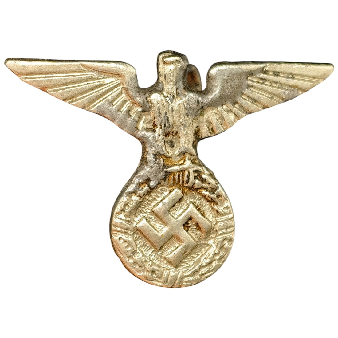 Third Reich Nazi NSDAP Eagle: A small stamped metal eagle insignia with wings spread, standing atop a wreathed swastika, for helmet or cap application. Reverse shows a small maker's roundel stamp, though the maker's name is not