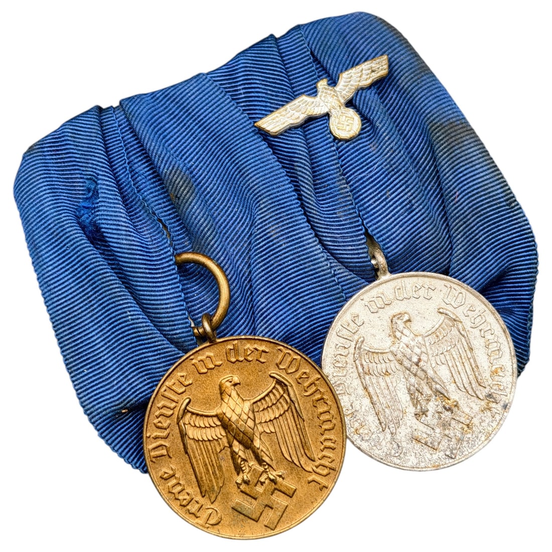 Third Reich Nazi Wehrmacht Service Medal Bar: A mounted medal bar featuring two Wehrmacht Dienstauszeichnung (Long Service) medals on blue moiré ribbon, with a small Wehrmacht Heer eagle device atop the mount. Both medals bear the inscription "T