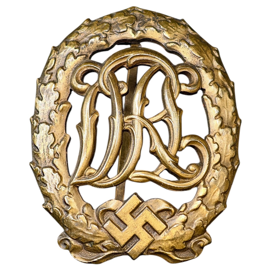 DRL Badge in Bronze – Third Reich Nazi Era Badge: Bronze-finished DRL (Deutscher Reichsbund für Leibesübungen) sports proficiency badge, featuring an oak leaf wreath surrounding the DRL cipher over a mobile swastika device.