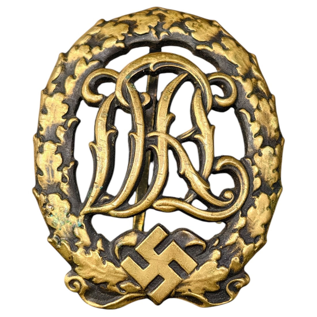 DRL Badge in Bronze – Third Reich Nazi Era Badge: Bronze-finished DRL (Deutscher Reichsbund für Leibesübungen) sports proficiency badge, featuring an oak leaf wreath surrounding the DRL cipher over a mobile swastika device.