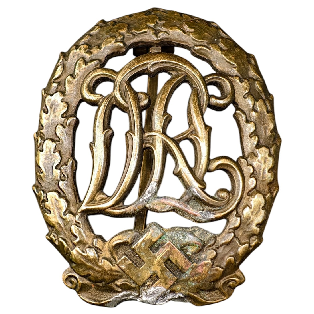 DRL Badge in Bronze – Third Reich Nazi Era Badge: Bronze-finished DRL (Deutscher Reichsbund für Leibesübungen) sports proficiency badge, featuring an oak leaf wreath surrounding the DRL cipher over a mobile swastika device.
