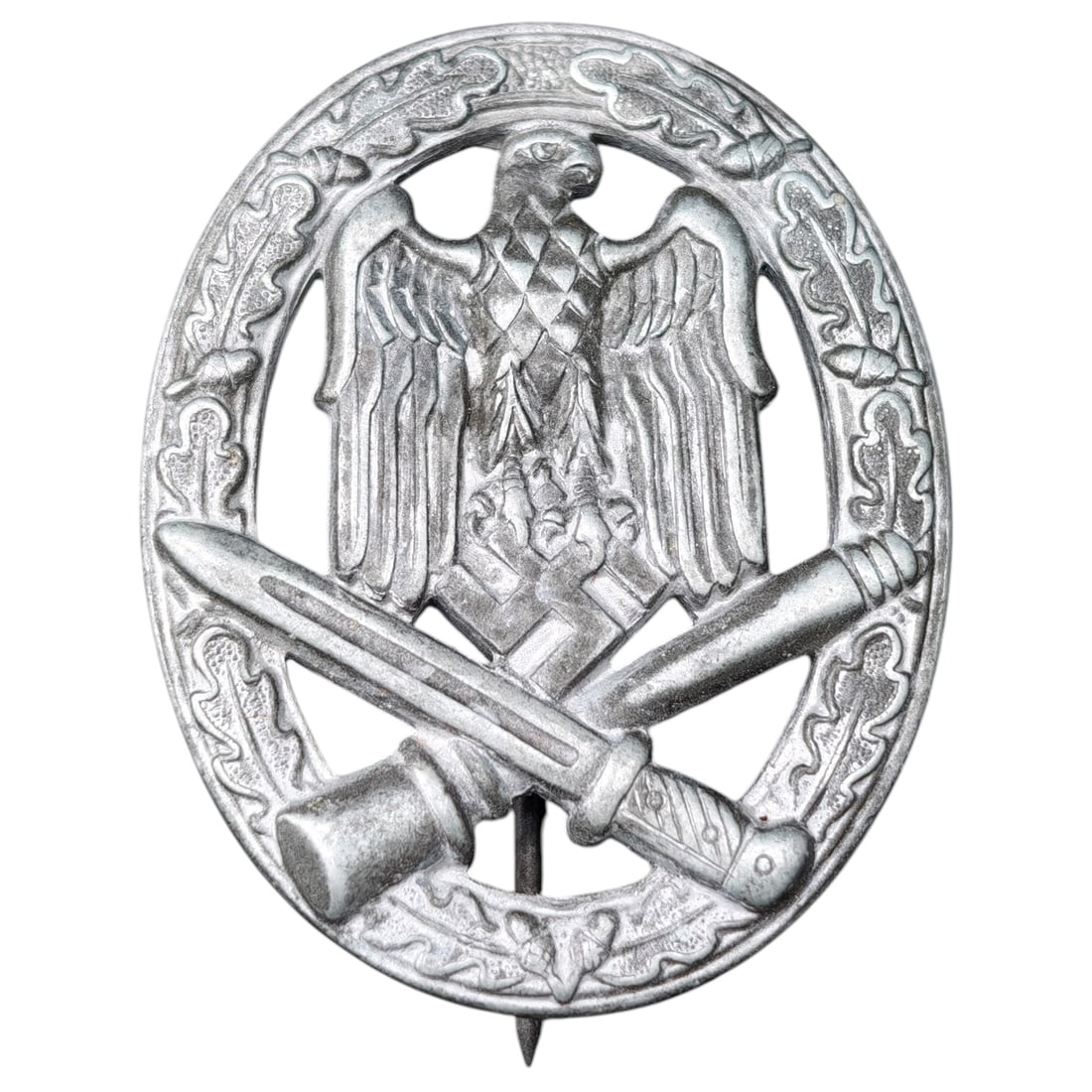 Third Reich Nazi General Assault Badge: A German WWII General Assault Badge featuring an oval wreath of oak leaves surrounding a national eagle clutching a mobile swastika, with crossed bayonet and stick grenade below. Die-struck in a white