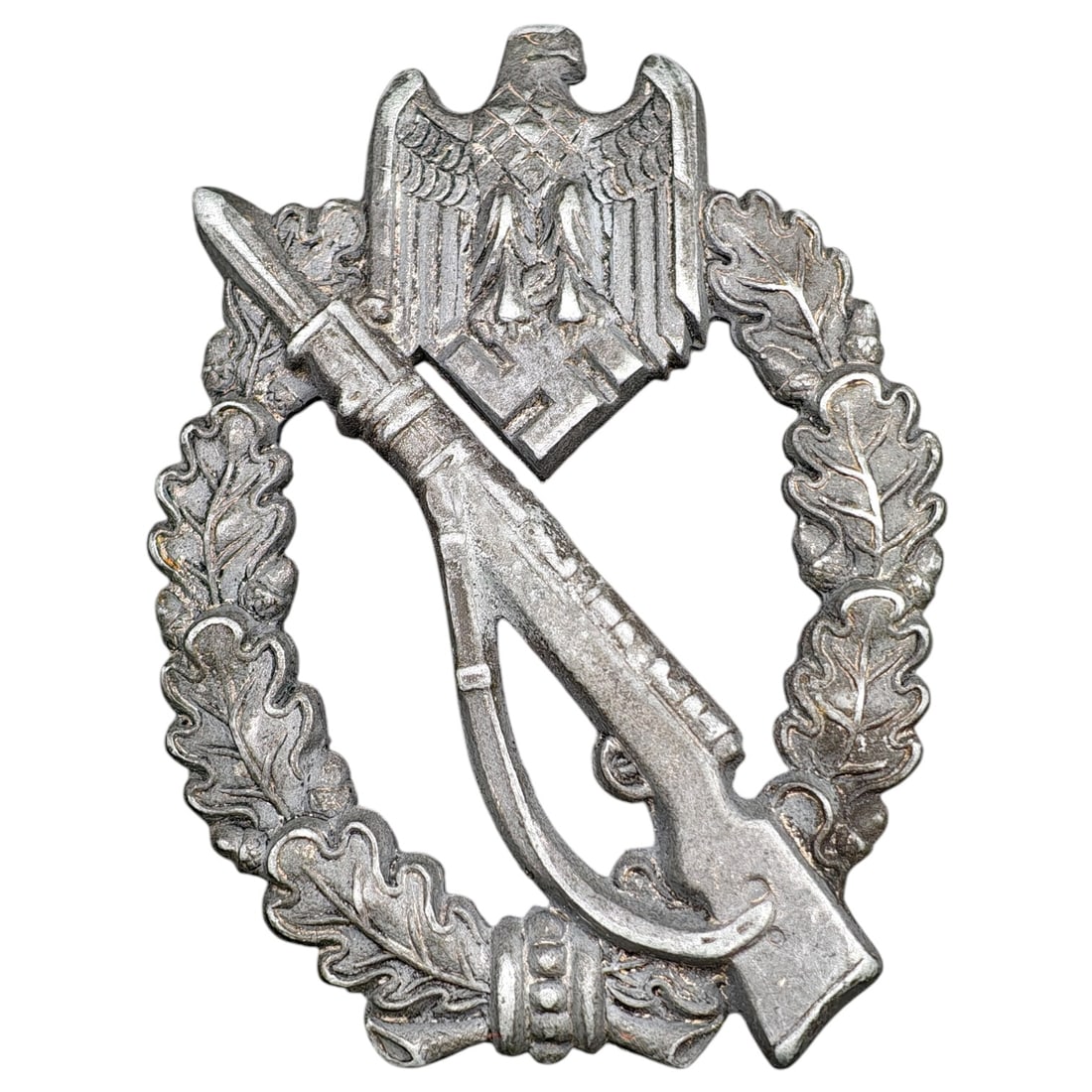 Third Reich Nazi Infantry Assault Badge: A badge in what appears to be silver-finish Infantre Sturmabzeichen featuring an eagle clutching a swastika above a K98 rifle, encircled by an oak leaf wreath. A partial maker mark is visible, though 
