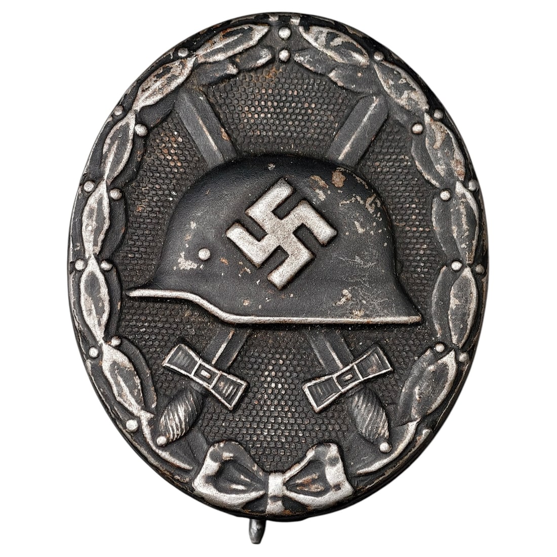 Wound Badge in Black – Third Reich Nazi Era Medal Badge: A Third Reich Wound Badge (Verwundetenabzeichen) in what appears to be black grade, depicting a steel helmet over a swastika, flanked by crossed swords, within a wreath border.