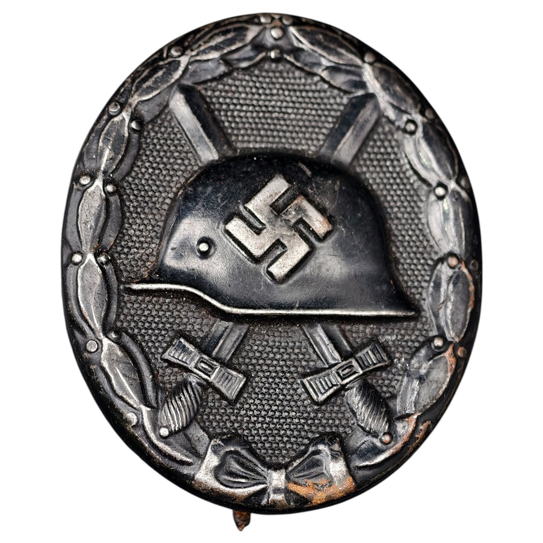 Wound Badge in Black – Third Reich Nazi Era Medal Badge: A Third Reich Wound Badge (Verwundetenabzeichen) in what appears to be black grade, depicting a steel helmet over a swastika, flanked by crossed swords, within a wreath border.