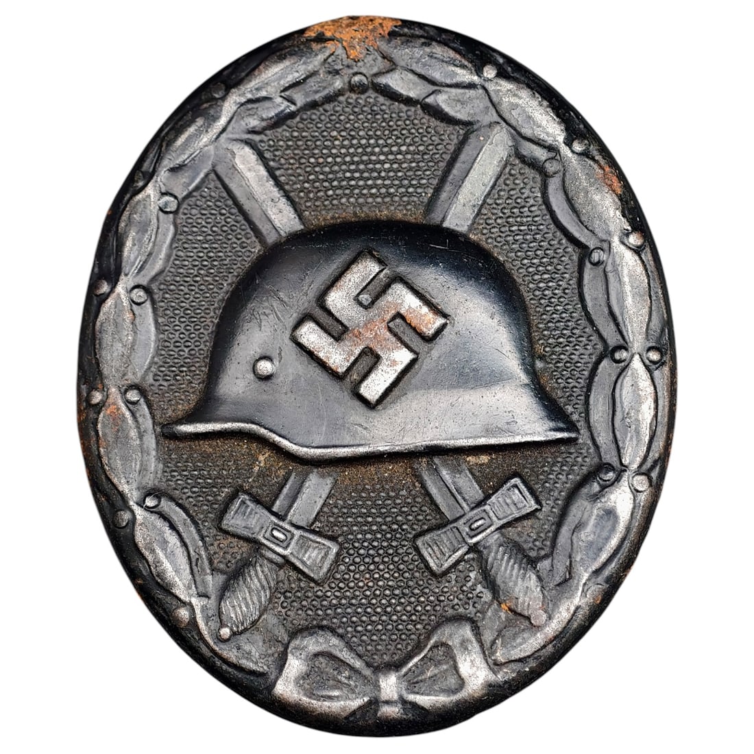 Wound Badge in Black – Third Reich Nazi Era Medal Badge: A Third Reich Wound Badge (Verwundetenabzeichen) in what appears to be black grade, depicting a steel helmet over a swastika, flanked by crossed swords, within a wreath border.