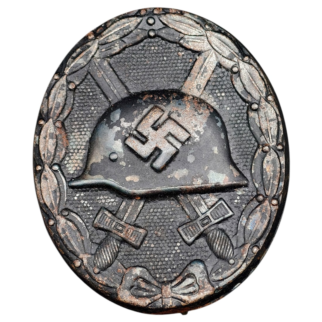 Wound Badge in Black – Third Reich Nazi Era Medal Badge: A Third Reich Wound Badge (Verwundetenabzeichen) in what appears to be black grade, depicting a steel helmet over a swastika, flanked by crossed swords, within a wreath border.