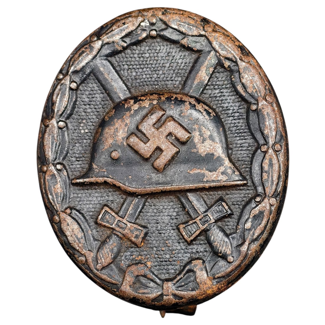Wound Badge in Black – Third Reich Nazi Era Medal Badge: A Third Reich Wound Badge (Verwundetenabzeichen) in what appears to be black grade, depicting a steel helmet over a swastika, flanked by crossed swords, within a wreath border.