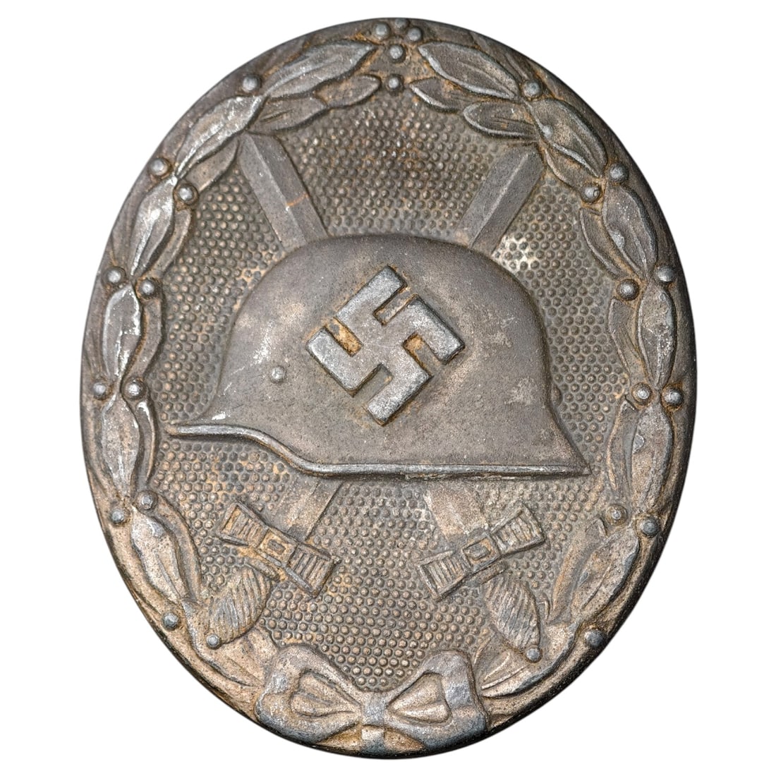 Third Reich Nazi Wound Badge in Silver: A Wound Badge in a silver grade featuring a stahlhelm over crossed swords with a swastika, surrounded by a laurel wreath tied at the base with a ribbon bow.