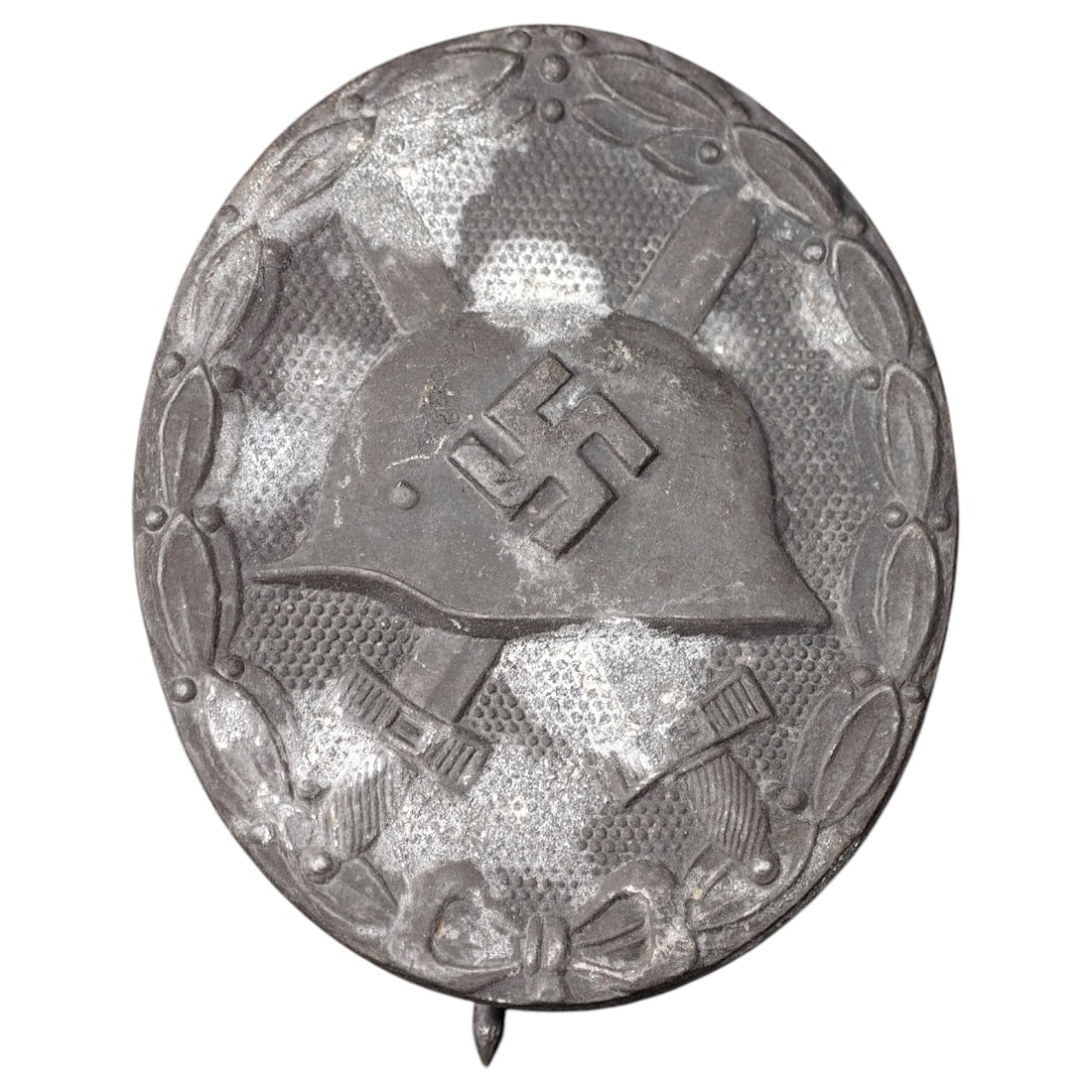 Third Reich Nazi Wound Badge in Silver: A Wound Badge in a silver grade featuring a stahlhelm over crossed swords with a swastika, surrounded by a laurel wreath tied at the base with a ribbon bow.