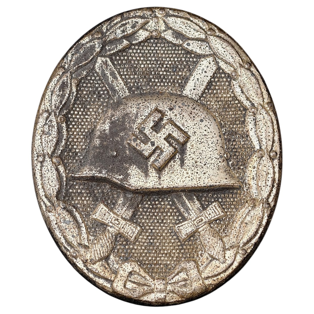 Third Reich Nazi Wound Badge in Silver: A Wound Badge in a silver grade featuring a stahlhelm over crossed swords with a swastika, surrounded by a laurel wreath tied at the base with a ribbon bow.