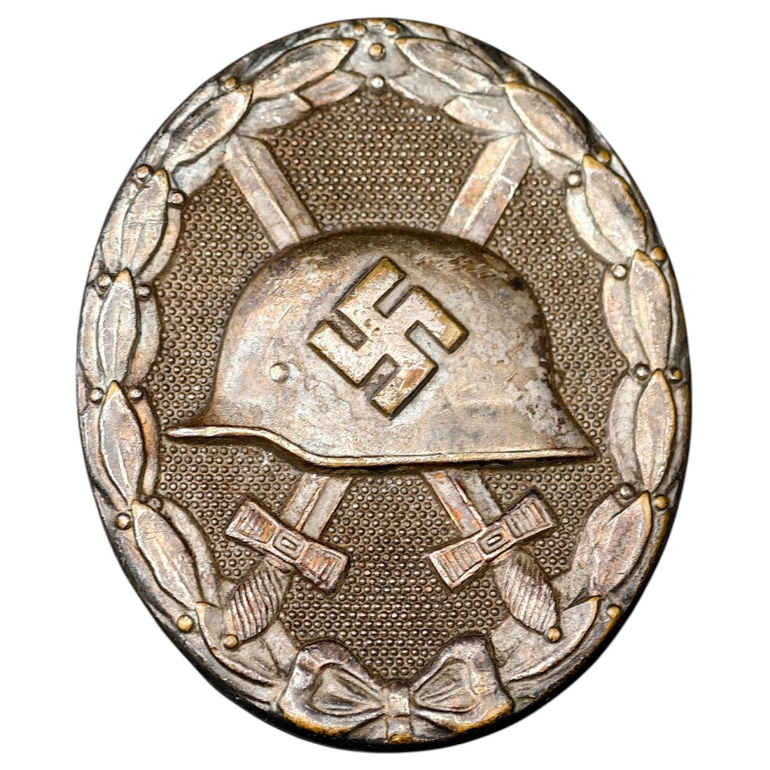 Third Reich Nazi Wound Badge in Silver: A Wound Badge in a silver grade featuring a stahlhelm over crossed swords with a swastika, surrounded by a laurel wreath tied at the base with a ribbon bow.