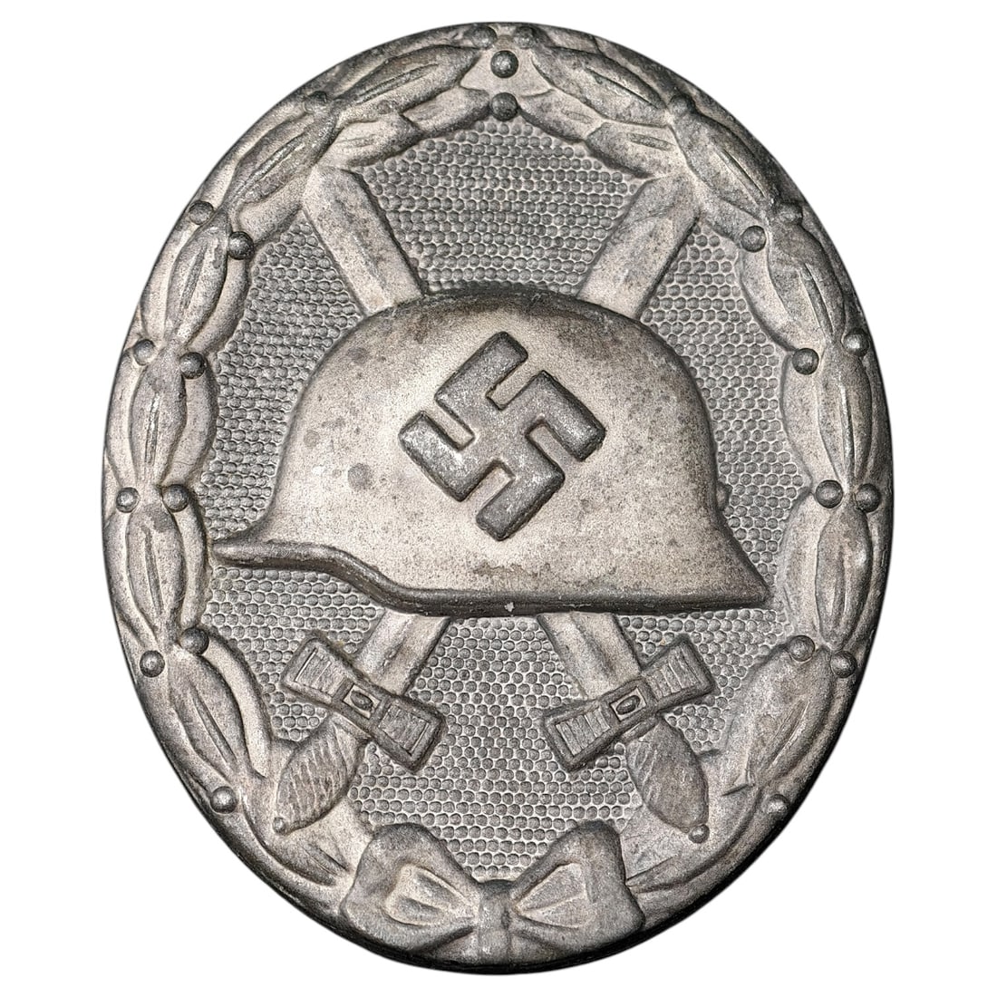 Third Reich Nazi Wound Badge in Silver: A Wound Badge in a silver grade featuring a stahlhelm over crossed swords with a swastika, surrounded by a laurel wreath tied at the base with a ribbon bow.