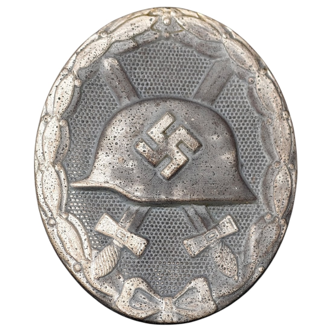 Third Reich Nazi Wound Badge in Silver: A Wound Badge in a silver grade featuring a stahlhelm over crossed swords with a swastika, surrounded by a laurel wreath tied at the base with a ribbon bow.