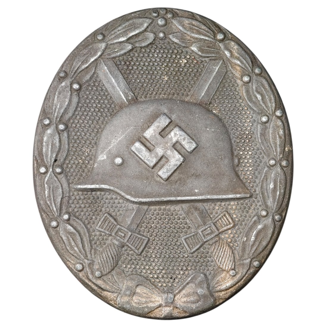 Third Reich Nazi Wound Badge in Silver: A Wound Badge in a silver grade featuring a stahlhelm over crossed swords with a swastika, surrounded by a laurel wreath tied at the base with a ribbon bow.