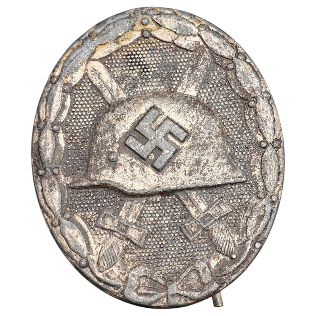 Third Reich Nazi Wound Badge in Silver: A Wound Badge in a silver grade featuring a stahlhelm over crossed swords with a swastika, surrounded by a laurel wreath tied at the base with a ribbon bow.