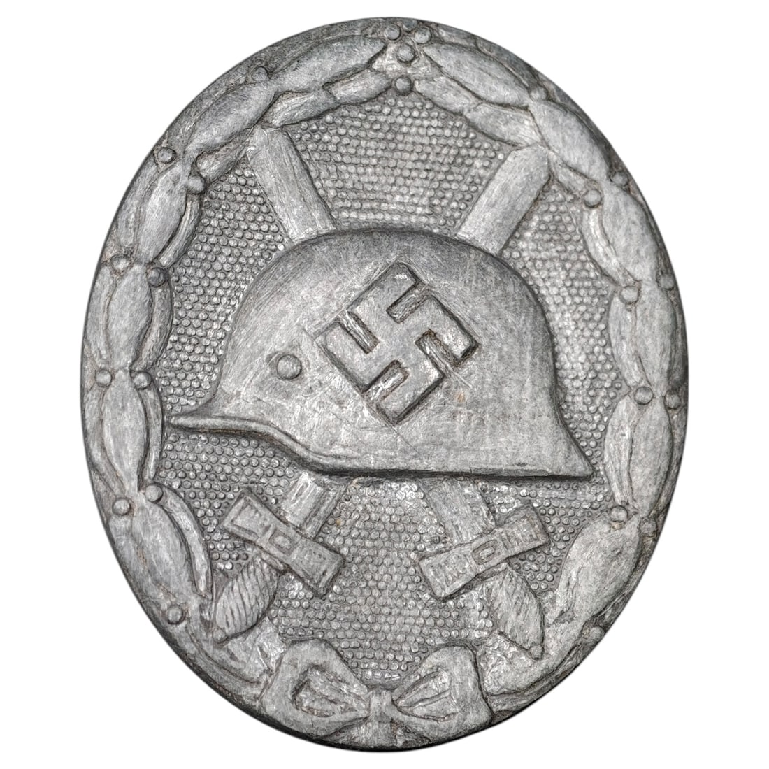 Third Reich Nazi Wound Badge in Silver: A Wound Badge in a silver grade featuring a stahlhelm over crossed swords with a swastika, surrounded by a laurel wreath tied at the base with a ribbon bow.