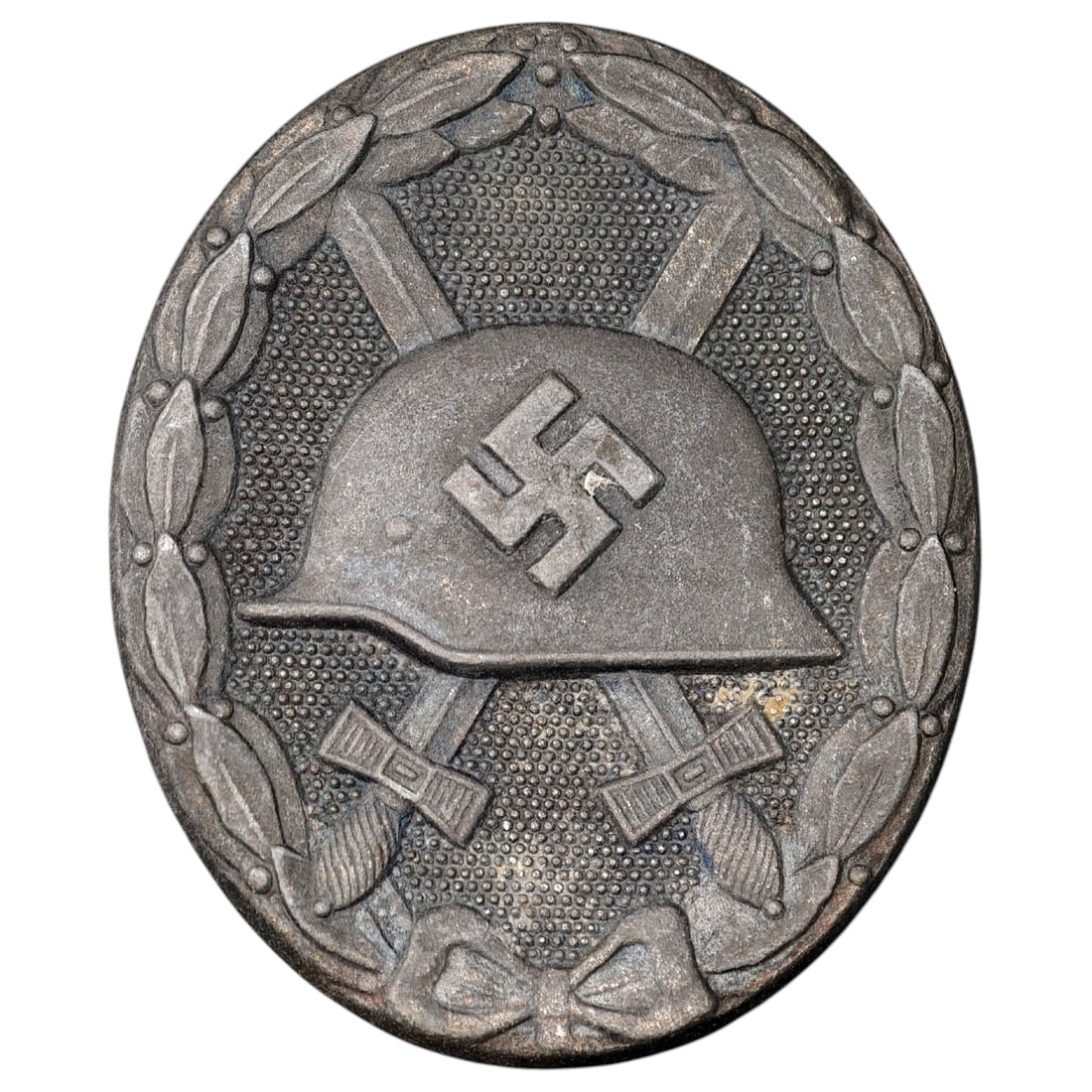 Third Reich Nazi Wound Badge in Silver: A Wound Badge in a silver grade featuring a stahlhelm over crossed swords with a swastika, surrounded by a laurel wreath tied at the base with a ribbon bow.