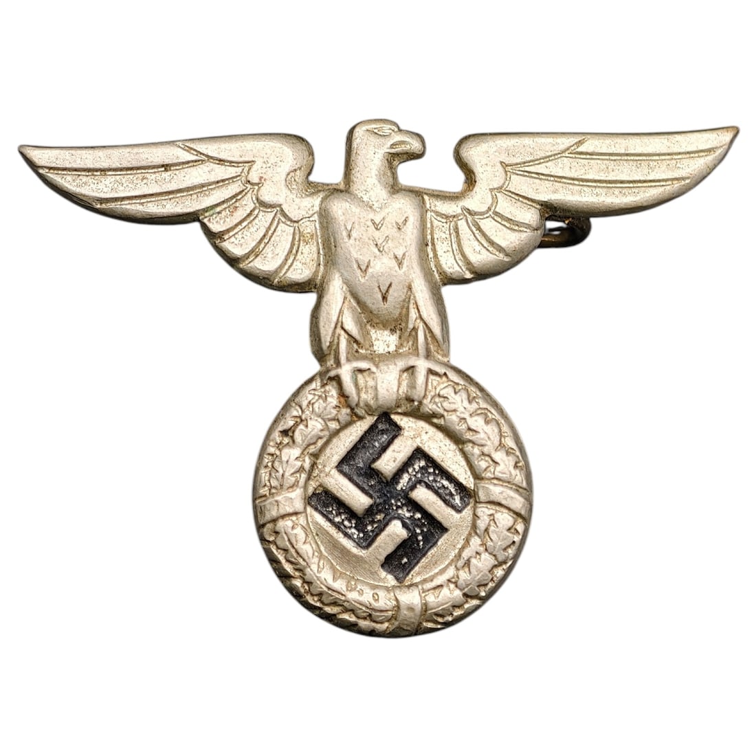 German WWII SA SS Eagle Pin: A metal eagle pin for SA/political, depicting an eagle with outstretched wings perched atop a wreathed roundel enclosing a swastika.