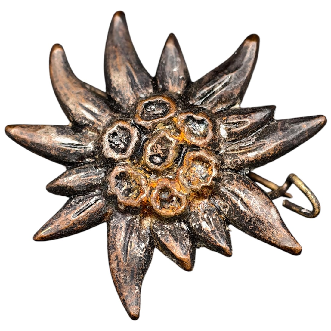 German WWII Edelweiss Cap Insignia: A pressed metal Edelweiss badge worn by German Gebirgsjäger (mountain troops), depicting the stylized flower with pointed petals and a beaded center. The metal appears to be believed to be a white me