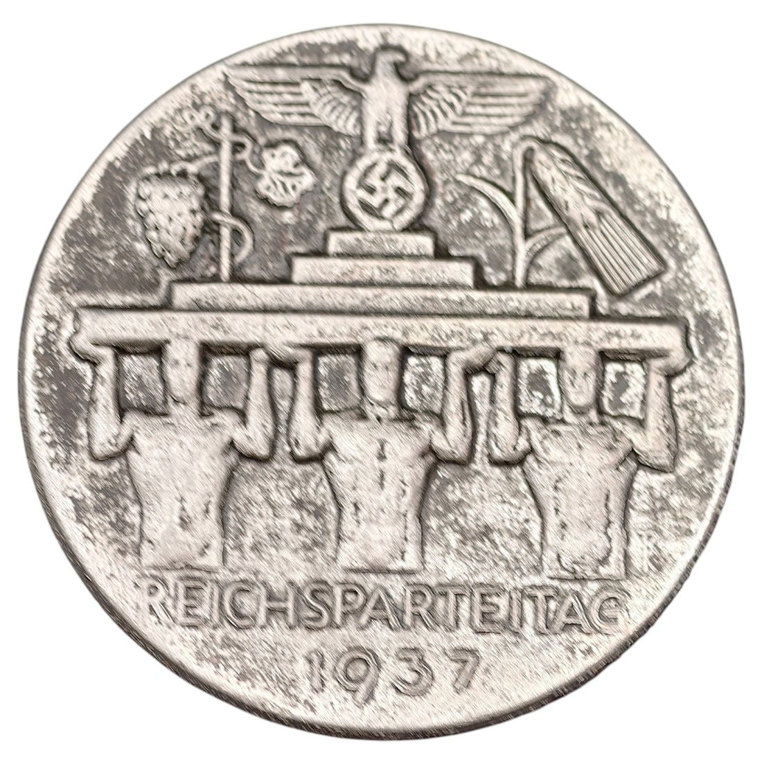 Third Reich Nazi Reichsparteitag 1937 Tinnie Badge: A pin-back commemorative tinnie for the Nuremberg Reichsparteitag (Nazi Party Rally Day) of 1937, depicting the Brandenburg Gate surmounted by a Party eagle over a stylized swastika, flanked by region
