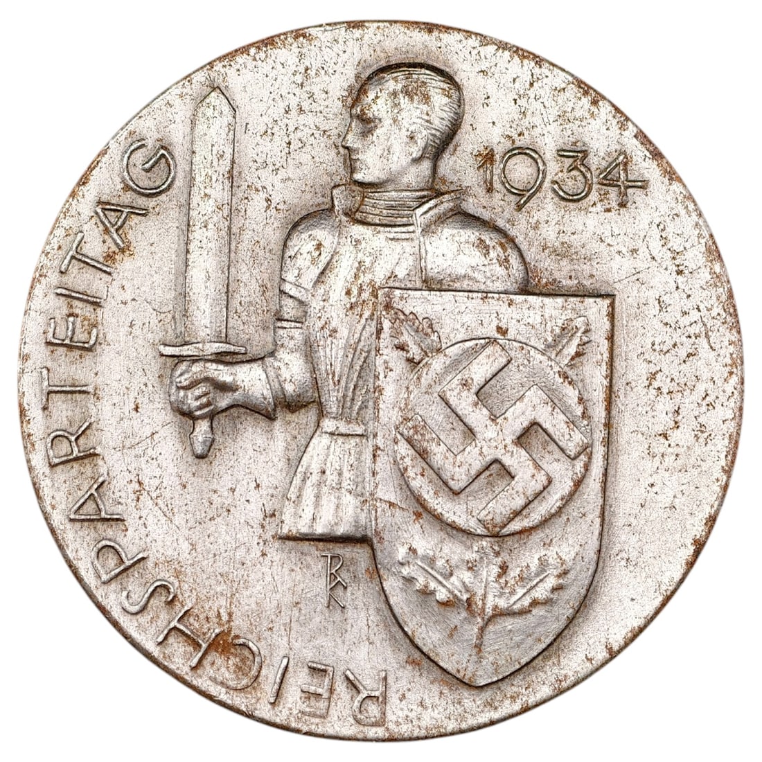German WWII Third Reich Reichsparteitag 1934 Badge: Round tinnie commemorating the 1934 Reichsparteitag (Nuremberg Rally), depicting a standard bearer figure holding a sword and a shield bearing a swastika device with oak leaf motif, with 'REICHSPARTEI