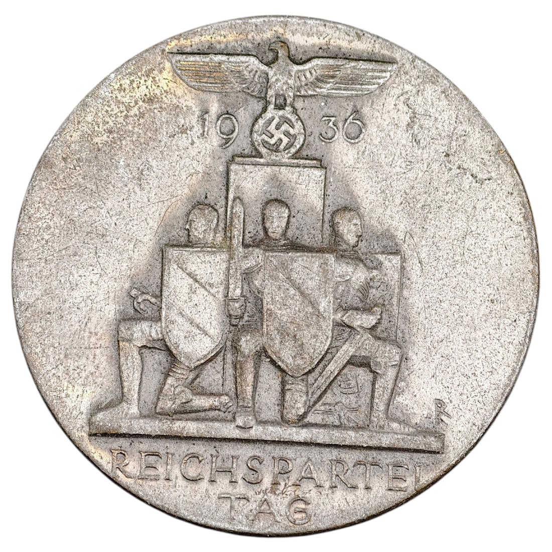 Third Reich Nazi Reichsparteitag Tinnie: A pin-back commemorative badge for the 1936 Reichsparteitag (Nazi Party Rally at Nuremberg), depicting a set of kneeling standard bearers with shields beneath a Party eagle and swastika, dated "1936" 